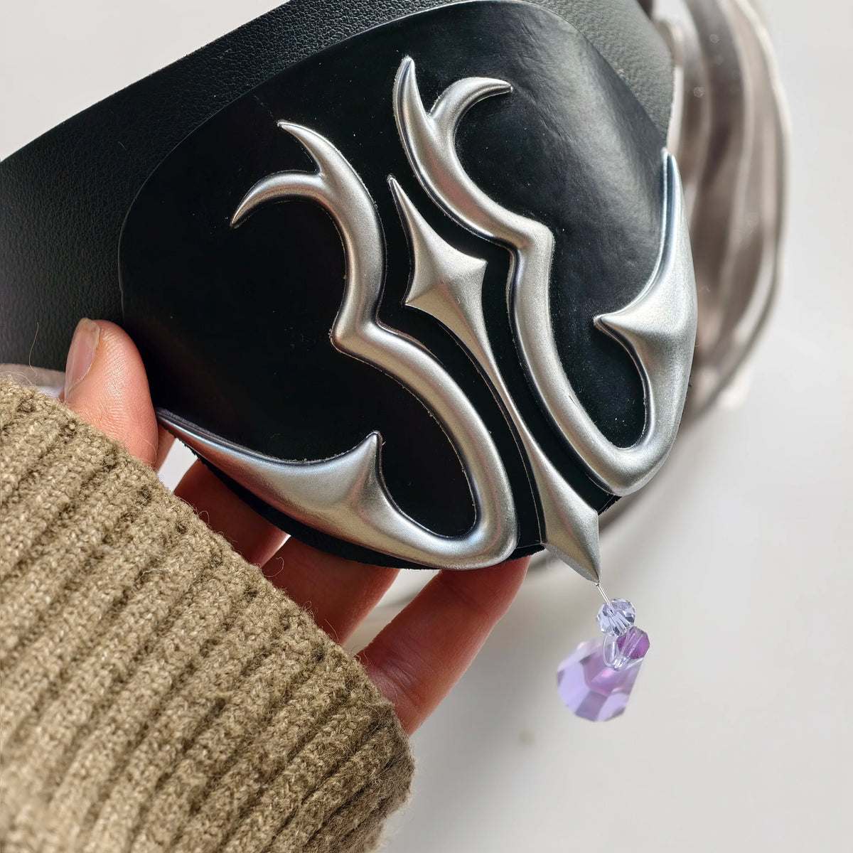 Black eye mask close-up with silver flame emblem and attached fabric strap