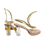Pair of nude pink high-heel sandals with gold curving straps, clear heels, red bead details